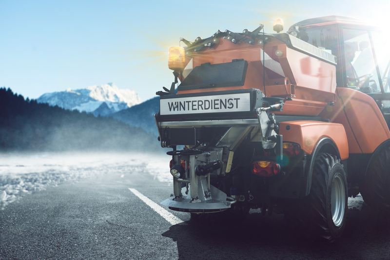 Streufahrzeug mit der Aufschrift Winterdienst vor Bergkulisse